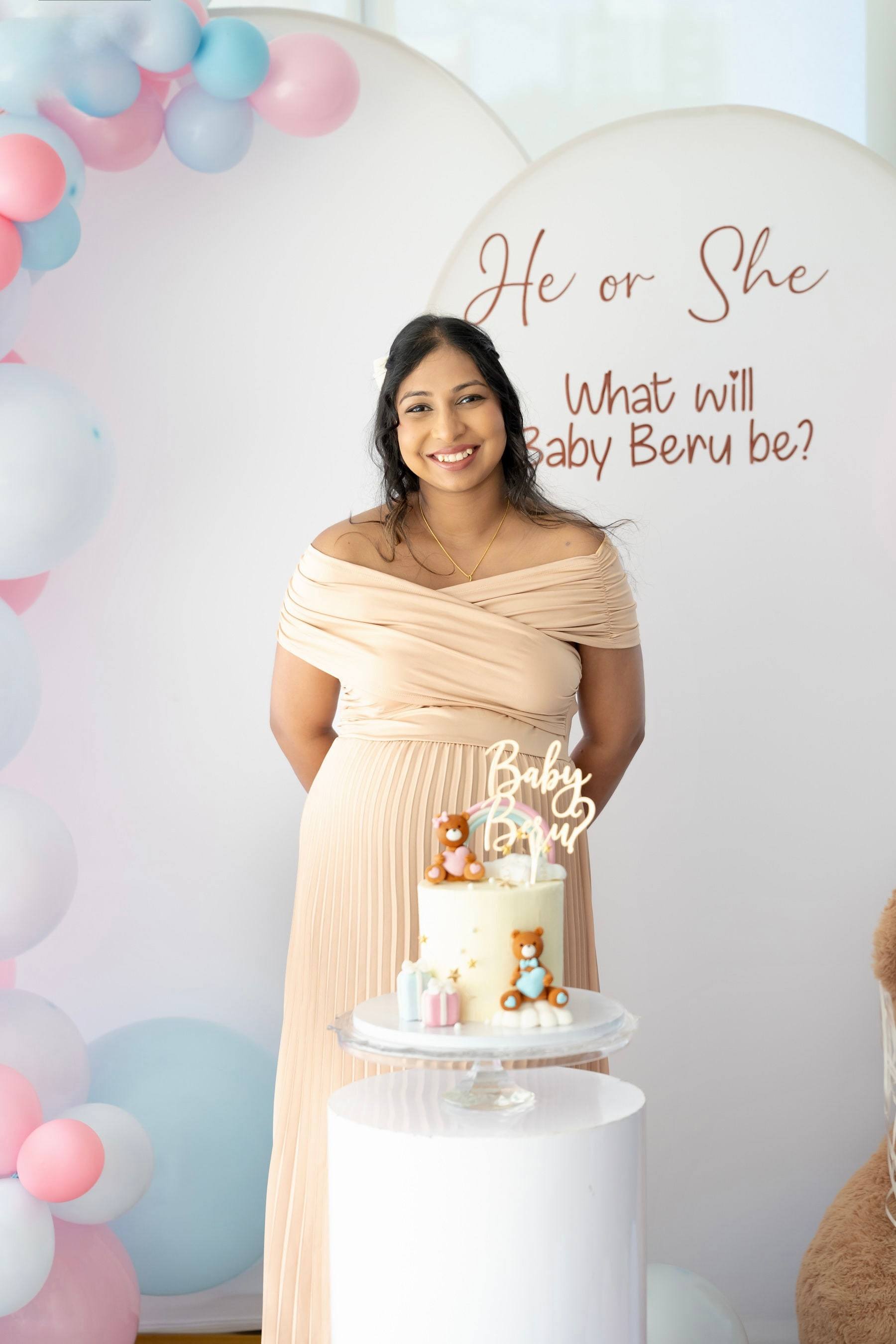 Expecting mother posing in front of a pink and blue balloon arch