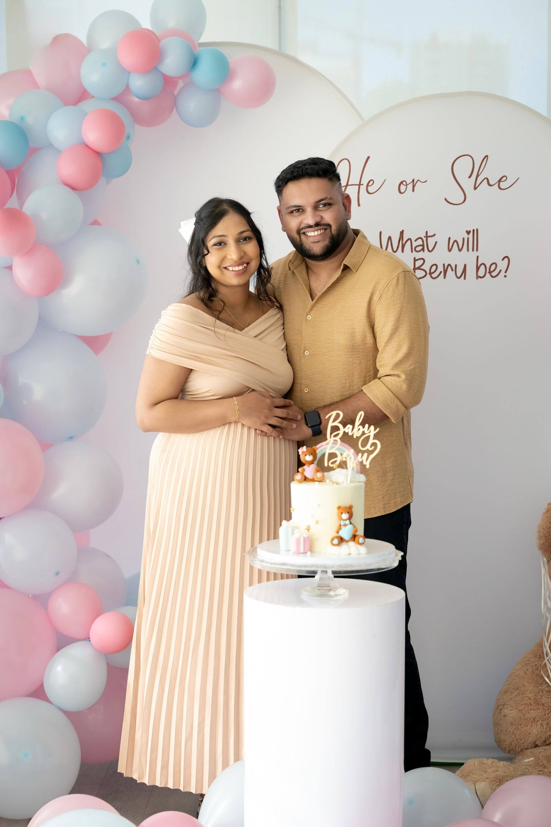 Expecting couple smiling together beside their gender reveal cake