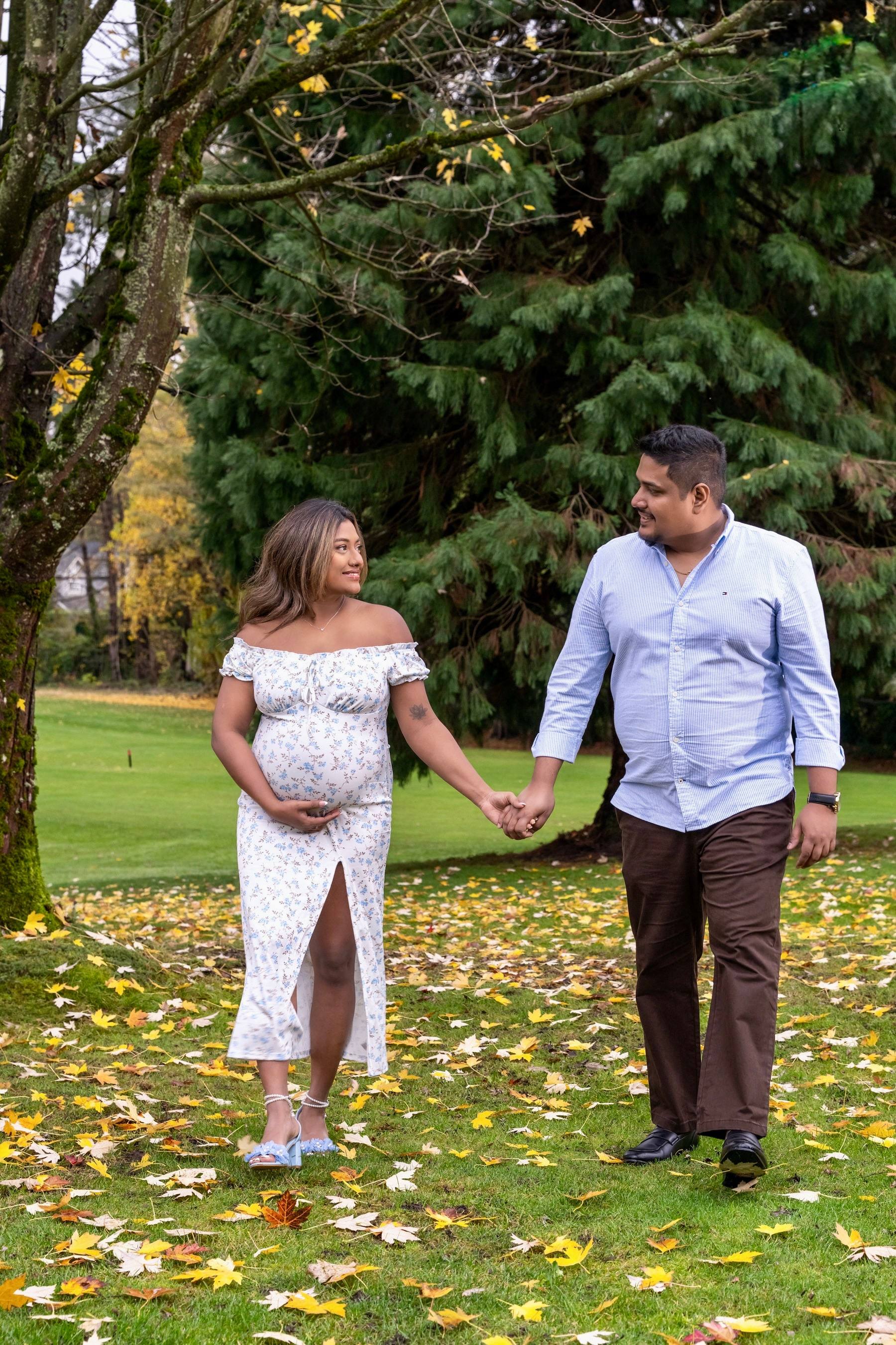 Expecting couple walking hand in hand across autumn leaves