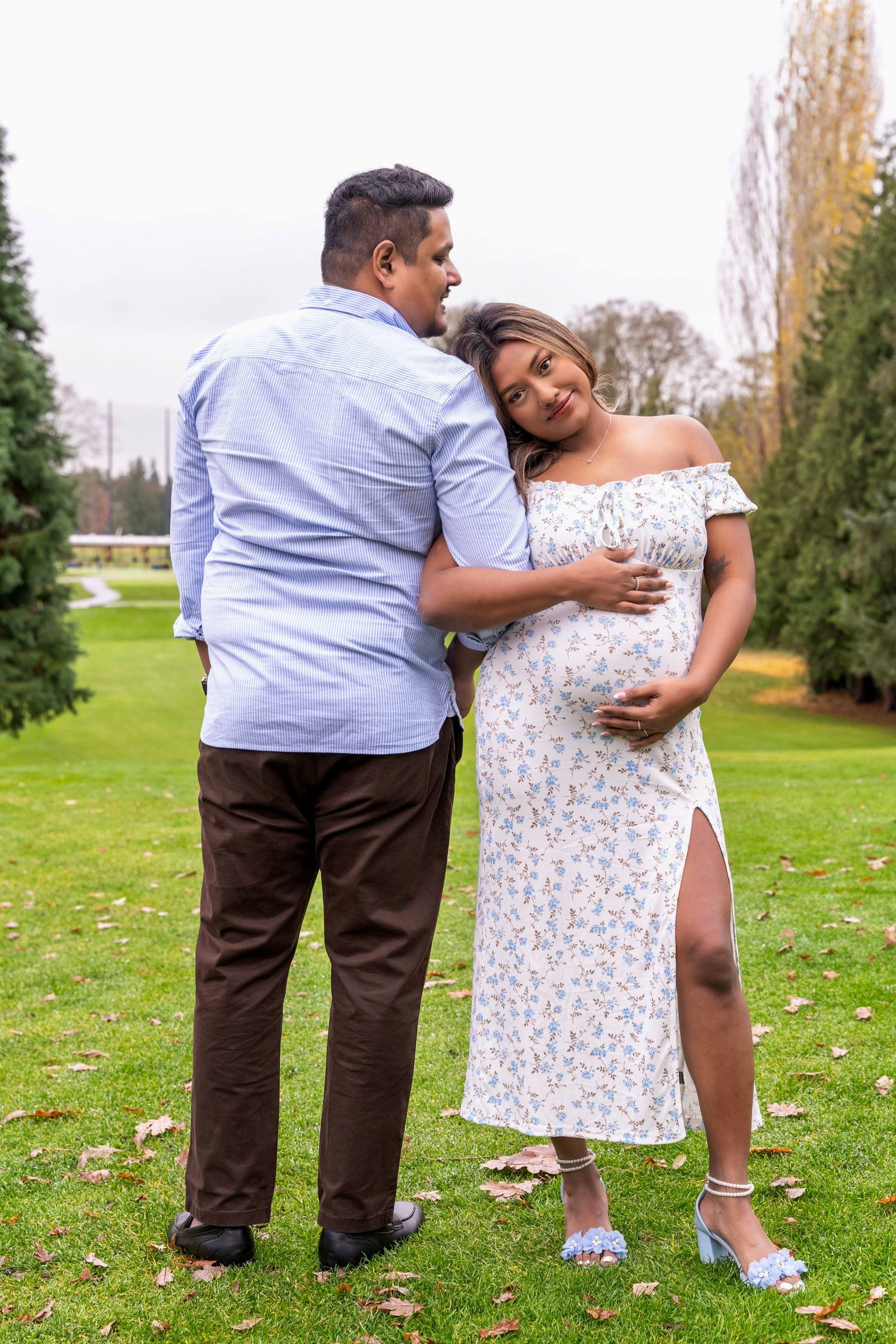 Father-to-be kissing his partner's head on a green lawn