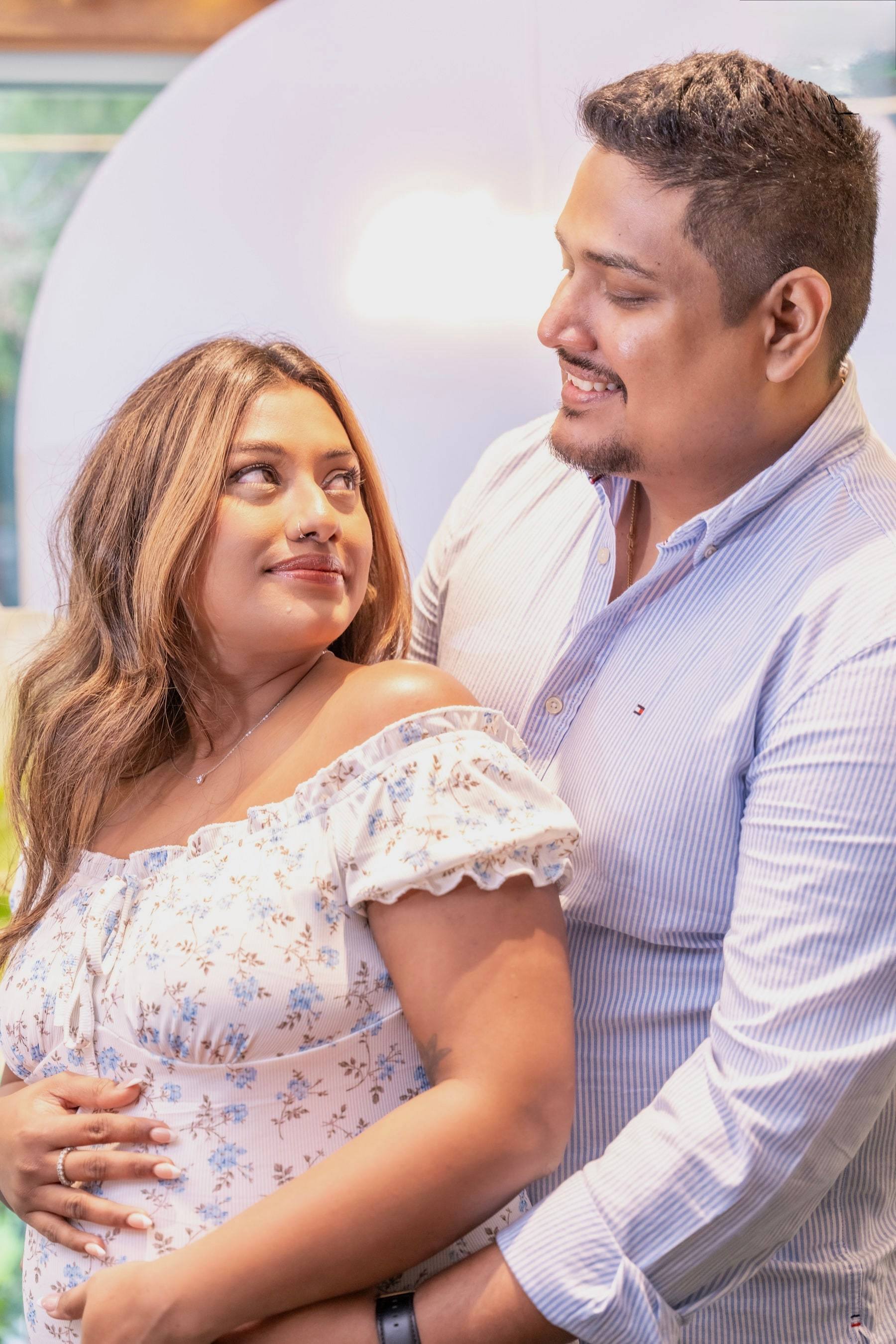 Expecting couple sharing a loving glance in front of a balloon backdrop