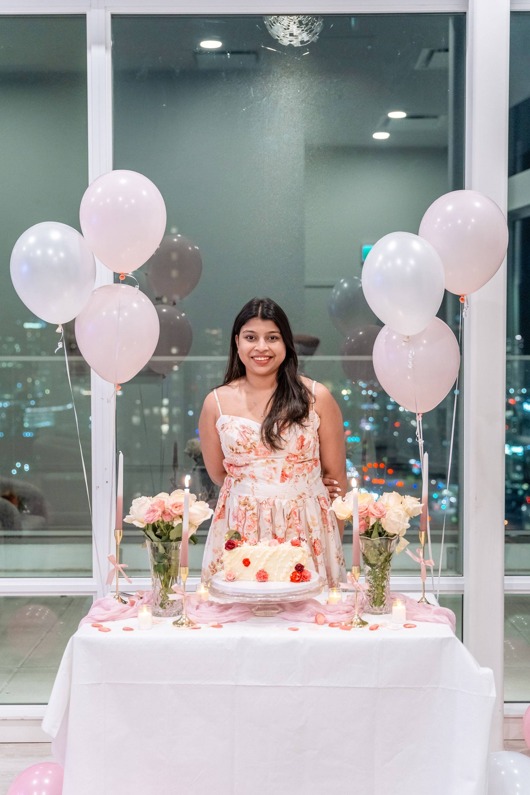 Birthday girl standing behind her cake table framed by pink balloons