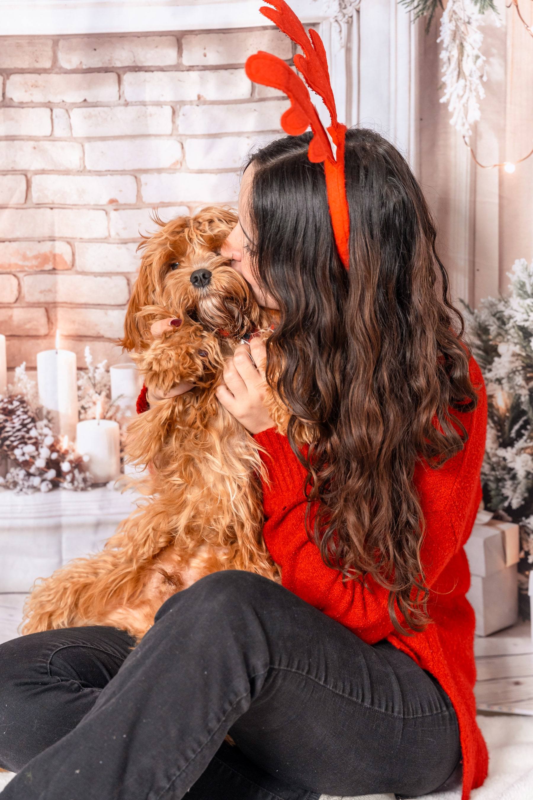 Woman kissing her dog in front of a festive white brick fireplace