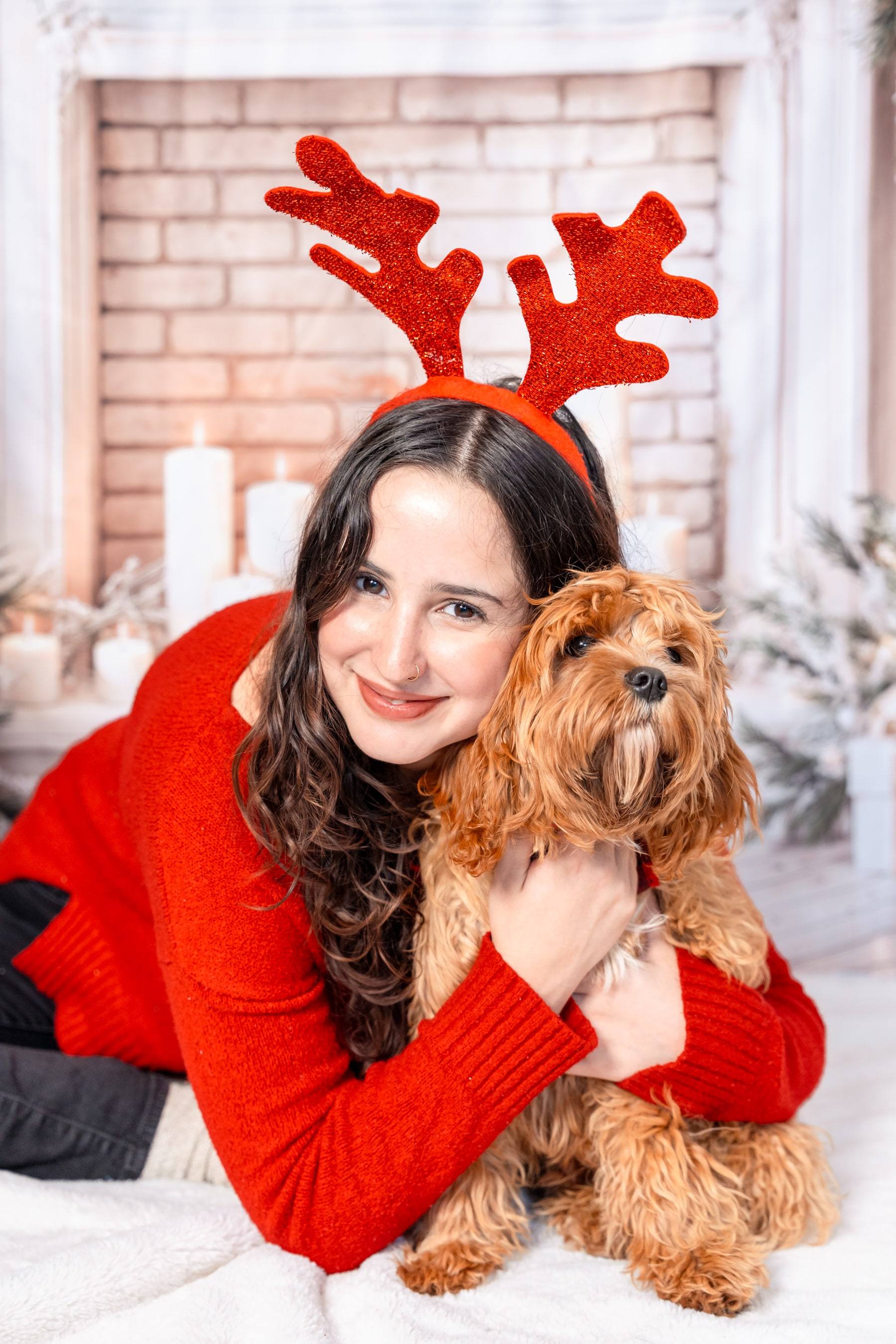 Woman lying on a faux fur rug hugging her dog in reindeer antlers