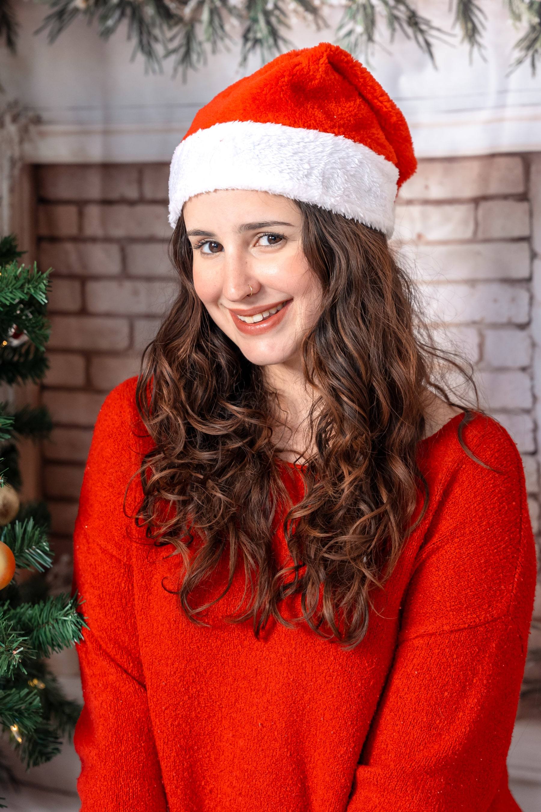 Close portrait of a woman in a Santa hat with a festive brick backdrop