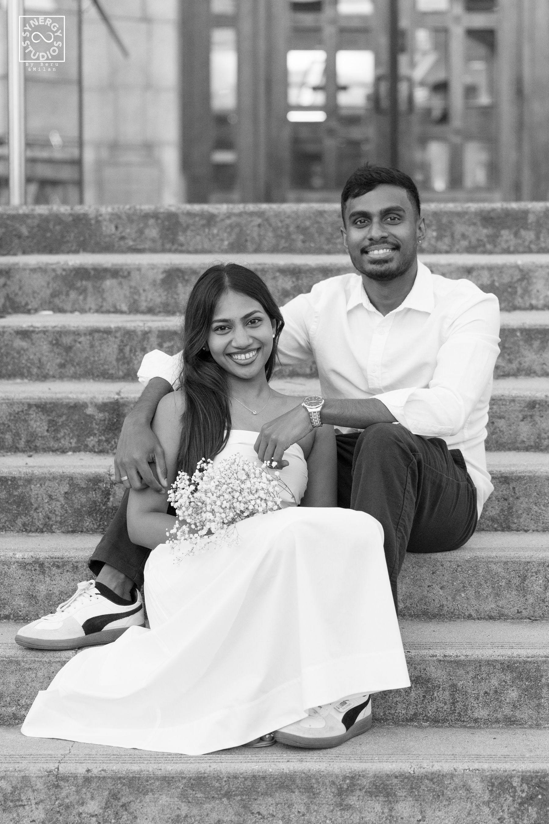 Black and white portrait of a smiling couple sitting on stone steps with a bouquet