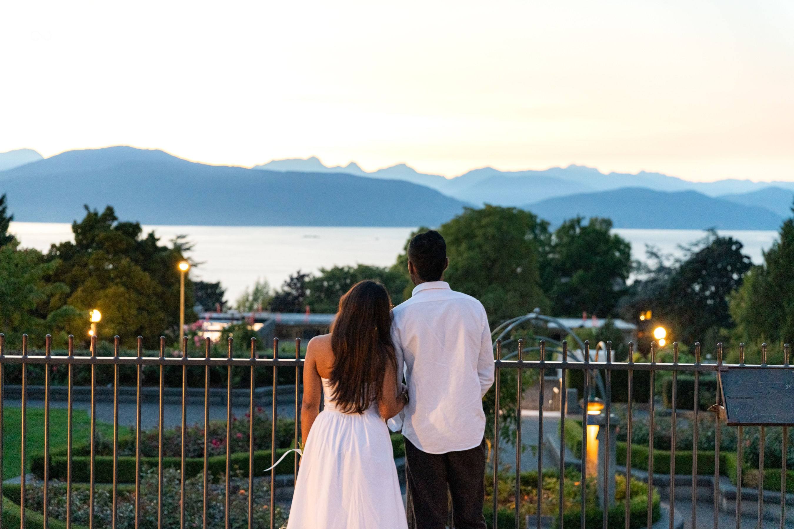 Couple from behind looking out over the water and mountains at dusk