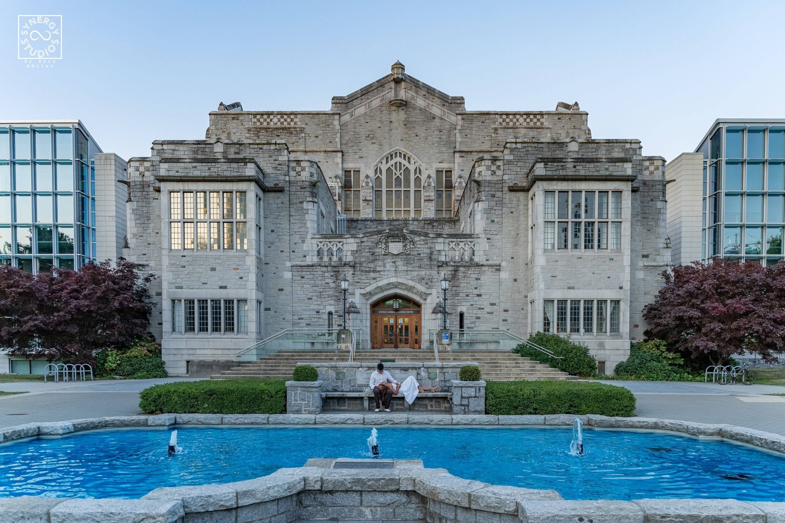 Wide view of a couple in front of a heritage stone building and reflecting fountain