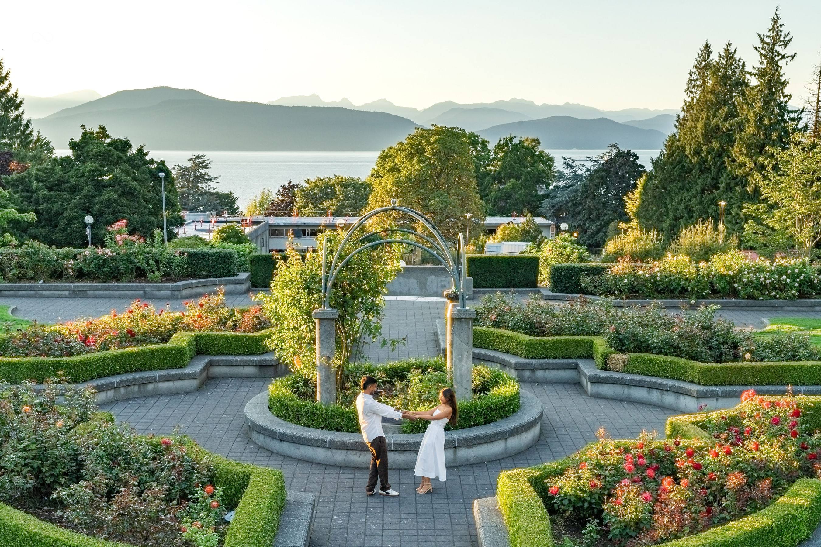 Couple dancing in a formal rose garden with the ocean and mountains in the distance
