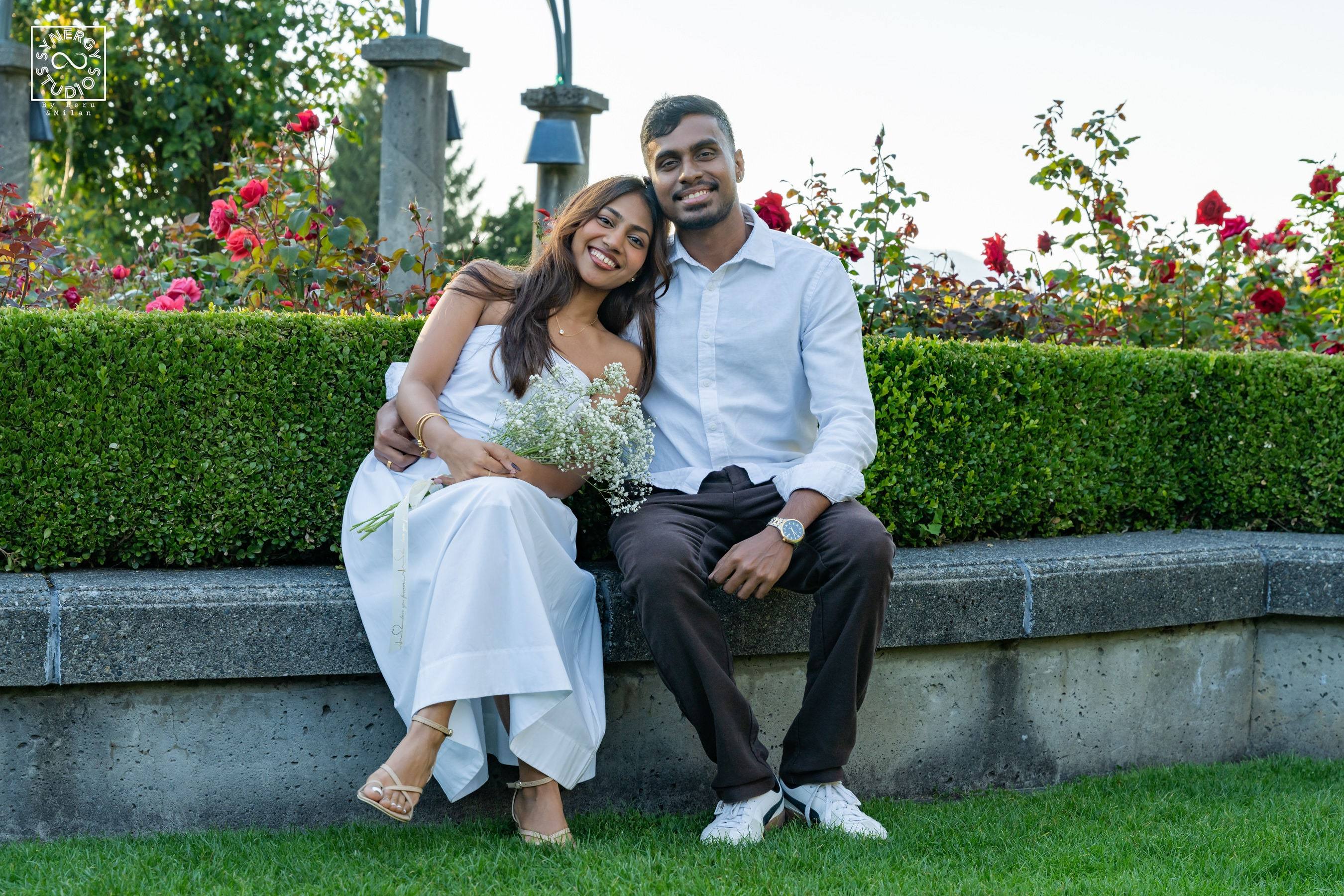 Laughing couple sitting on a garden ledge holding a bouquet of baby's breath