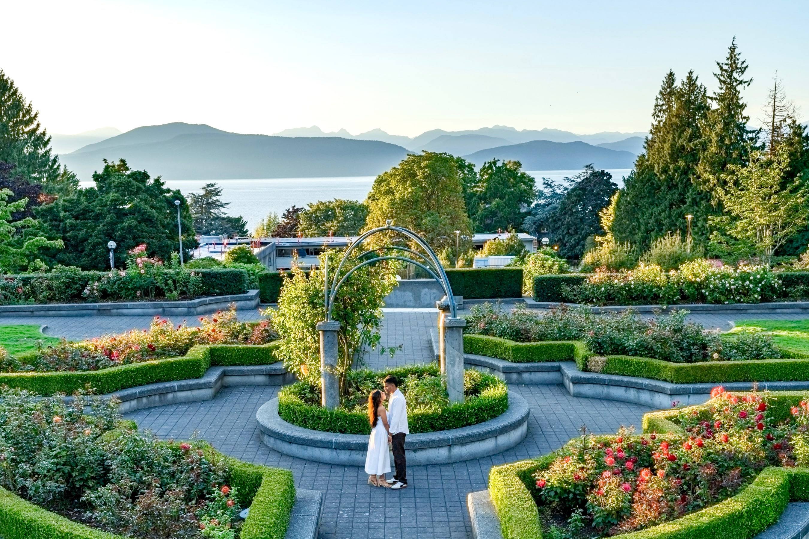 Couple standing in the centre of a manicured rose garden overlooking mountains