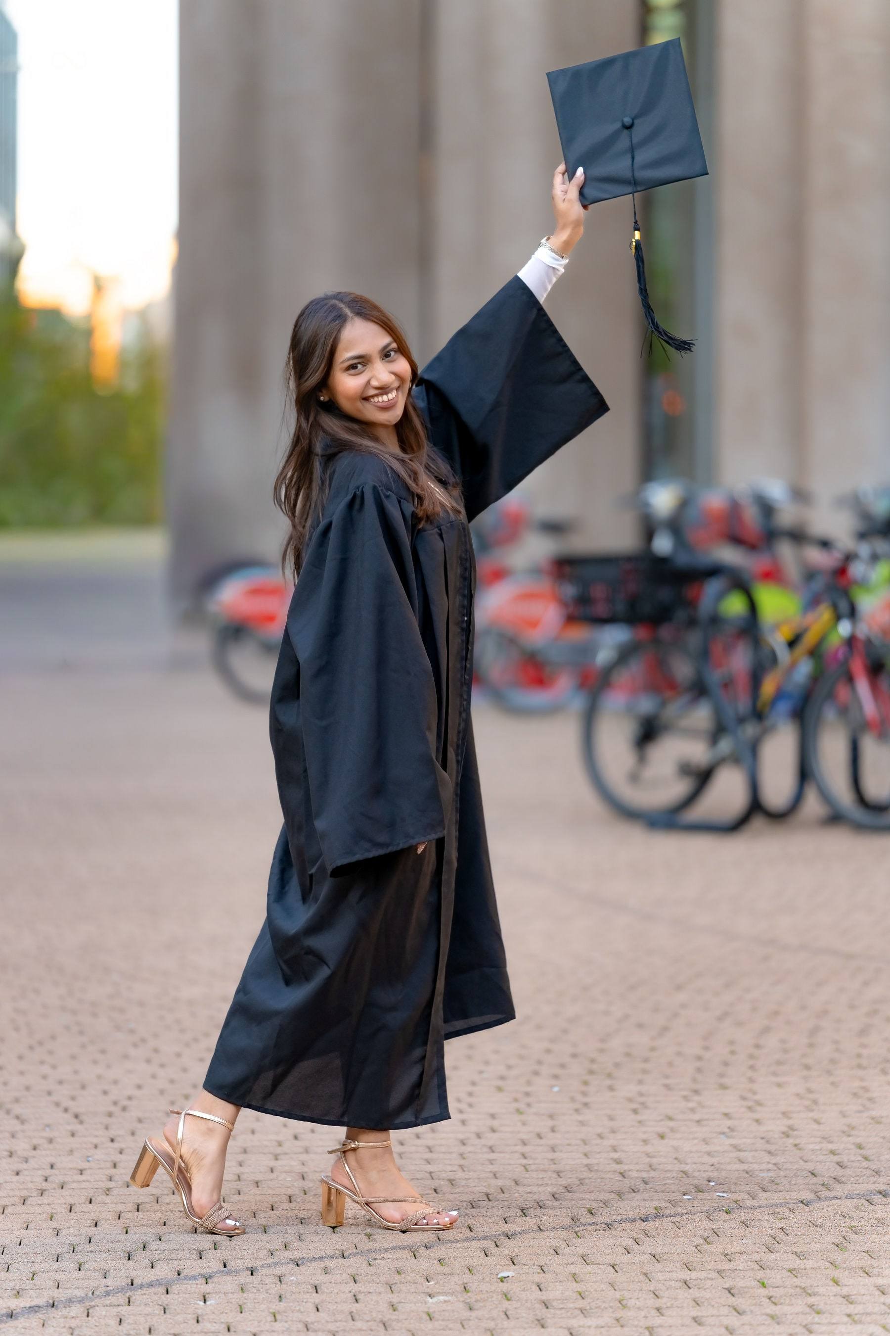 Graduate throwing her cap in the air between tall stone columns