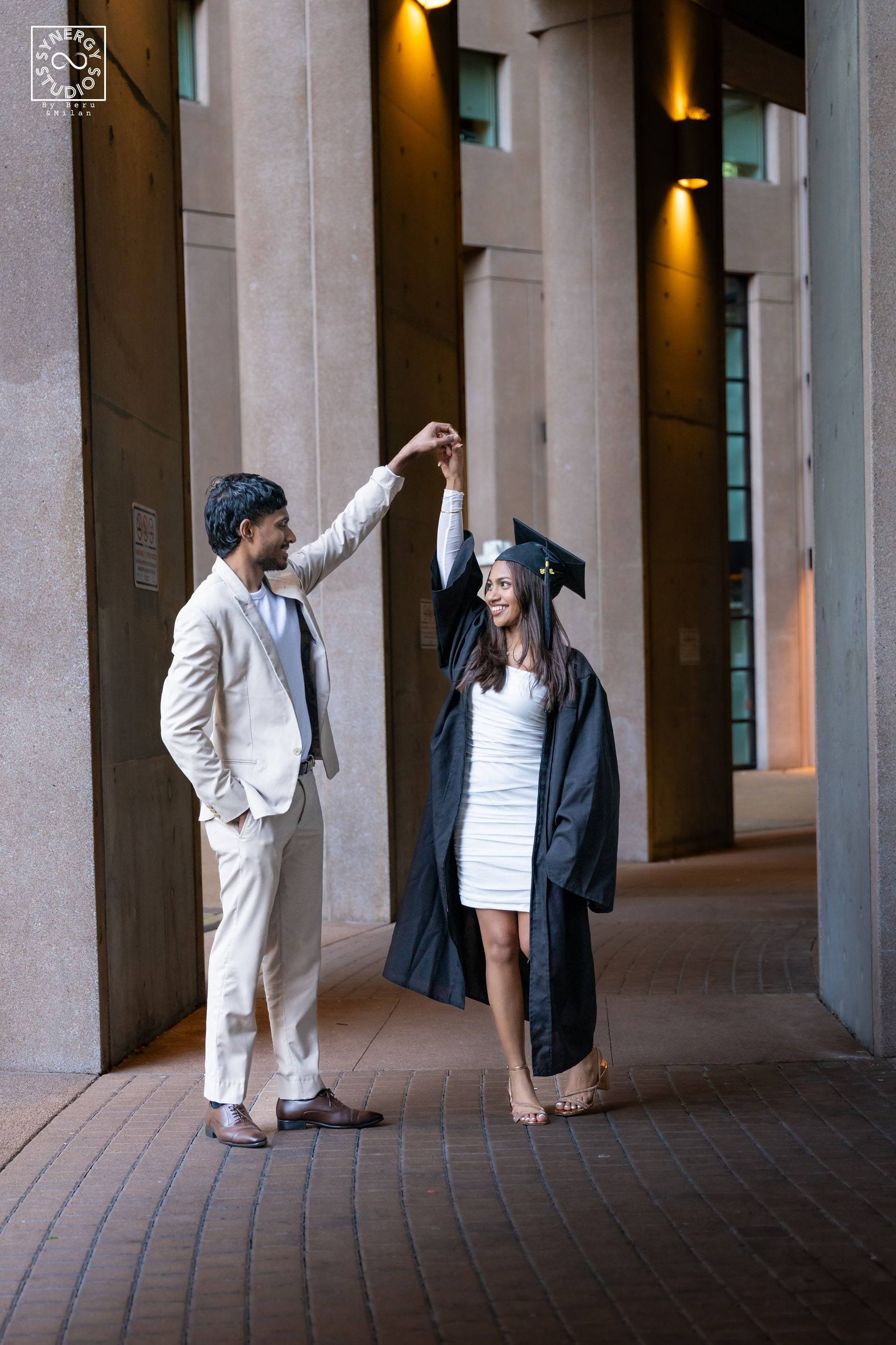 Graduate and her partner playfully holding the cap between building columns
