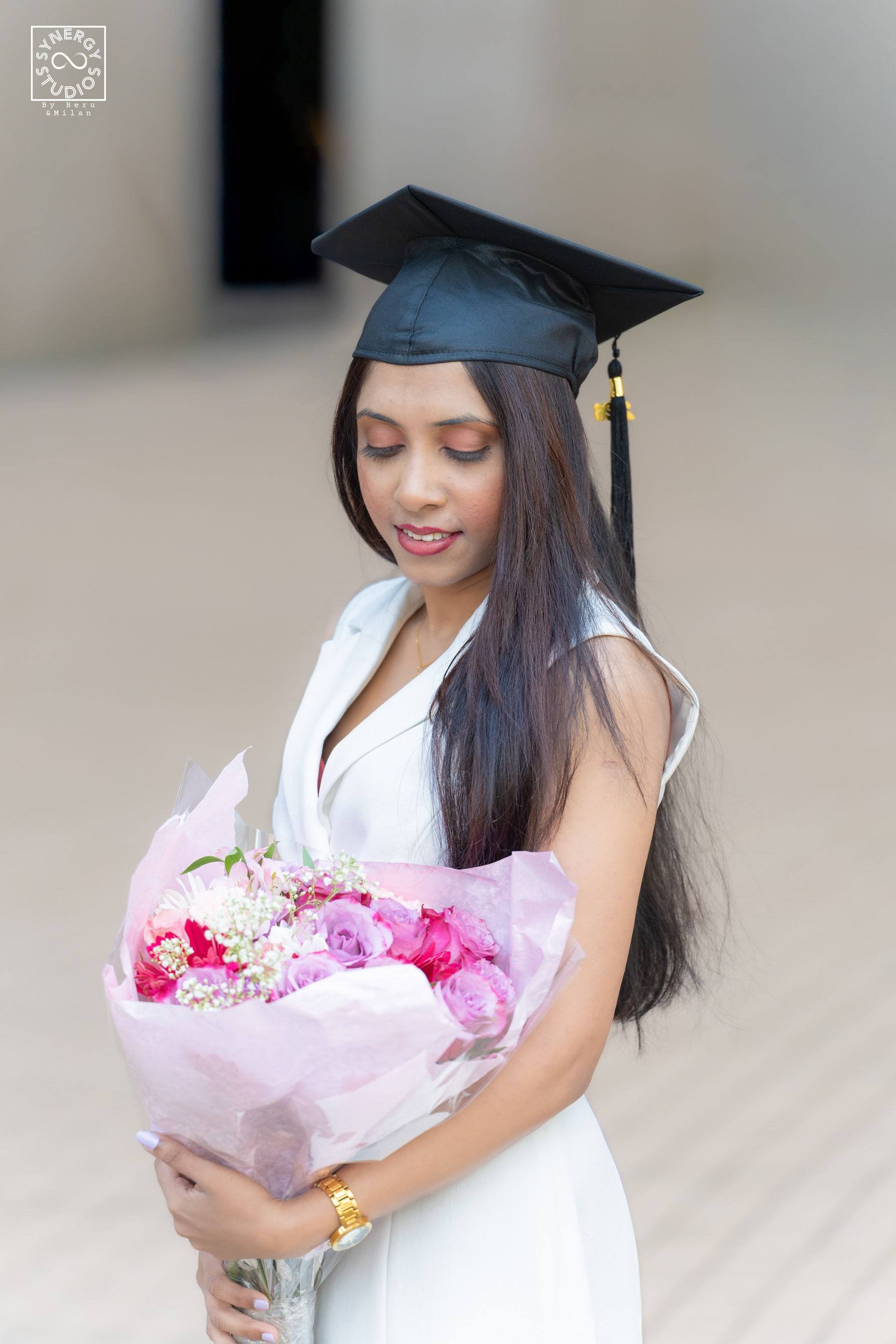 Graduate in a white dress and cap holding a pink bouquet