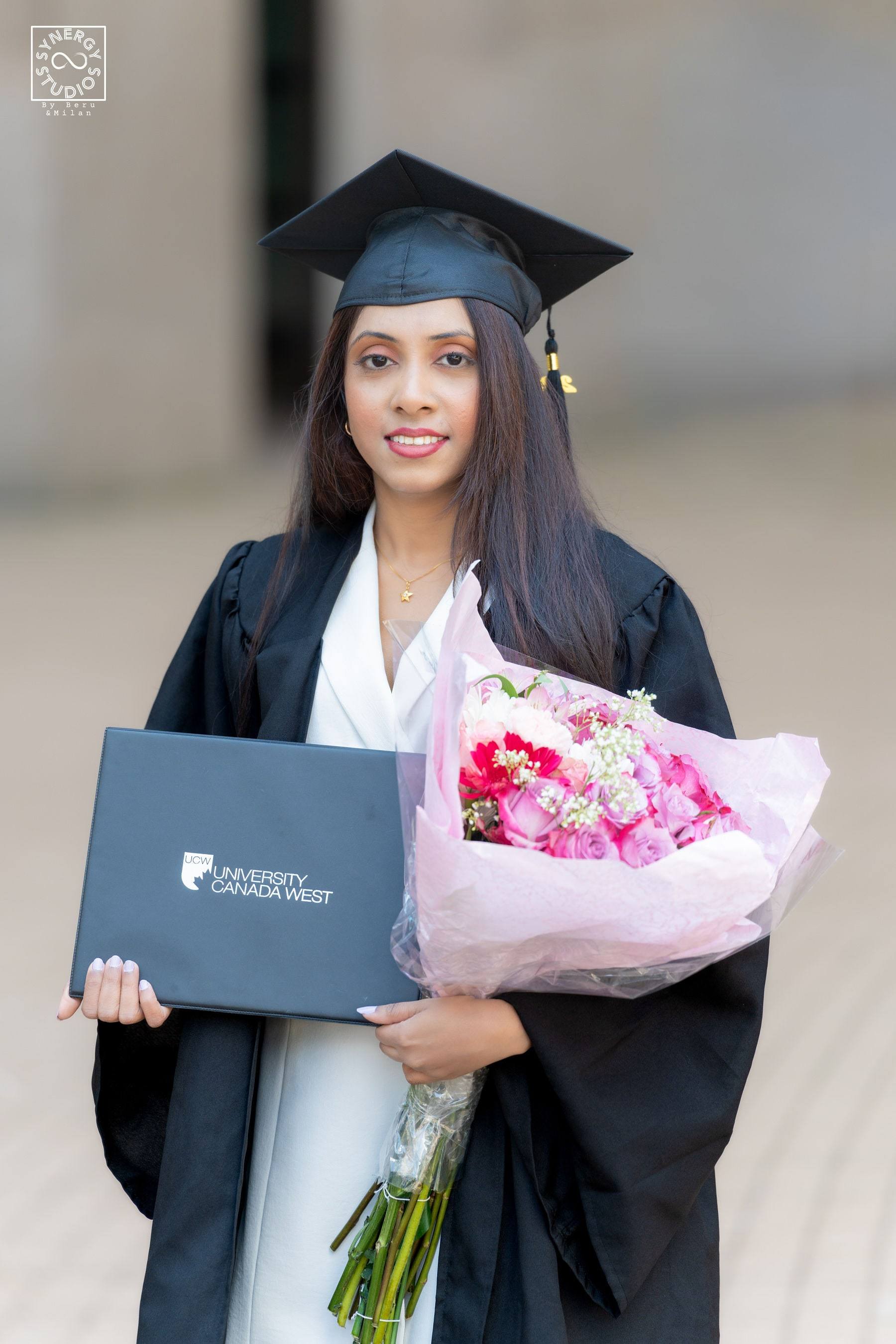 Graduate holding pink roses and her diploma in her black gown