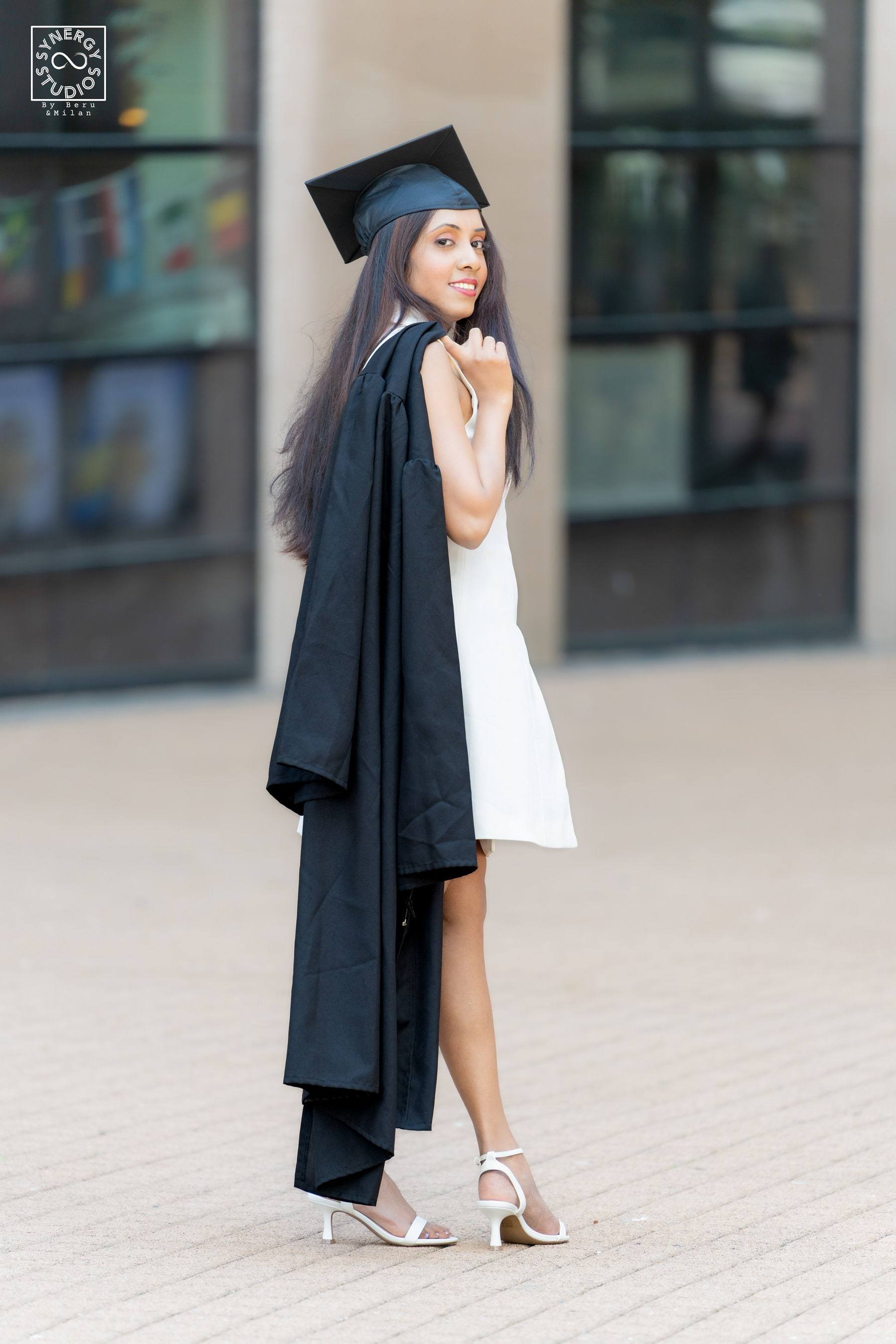 Graduate in a cap and gown looking over her shoulder in front of a modern building