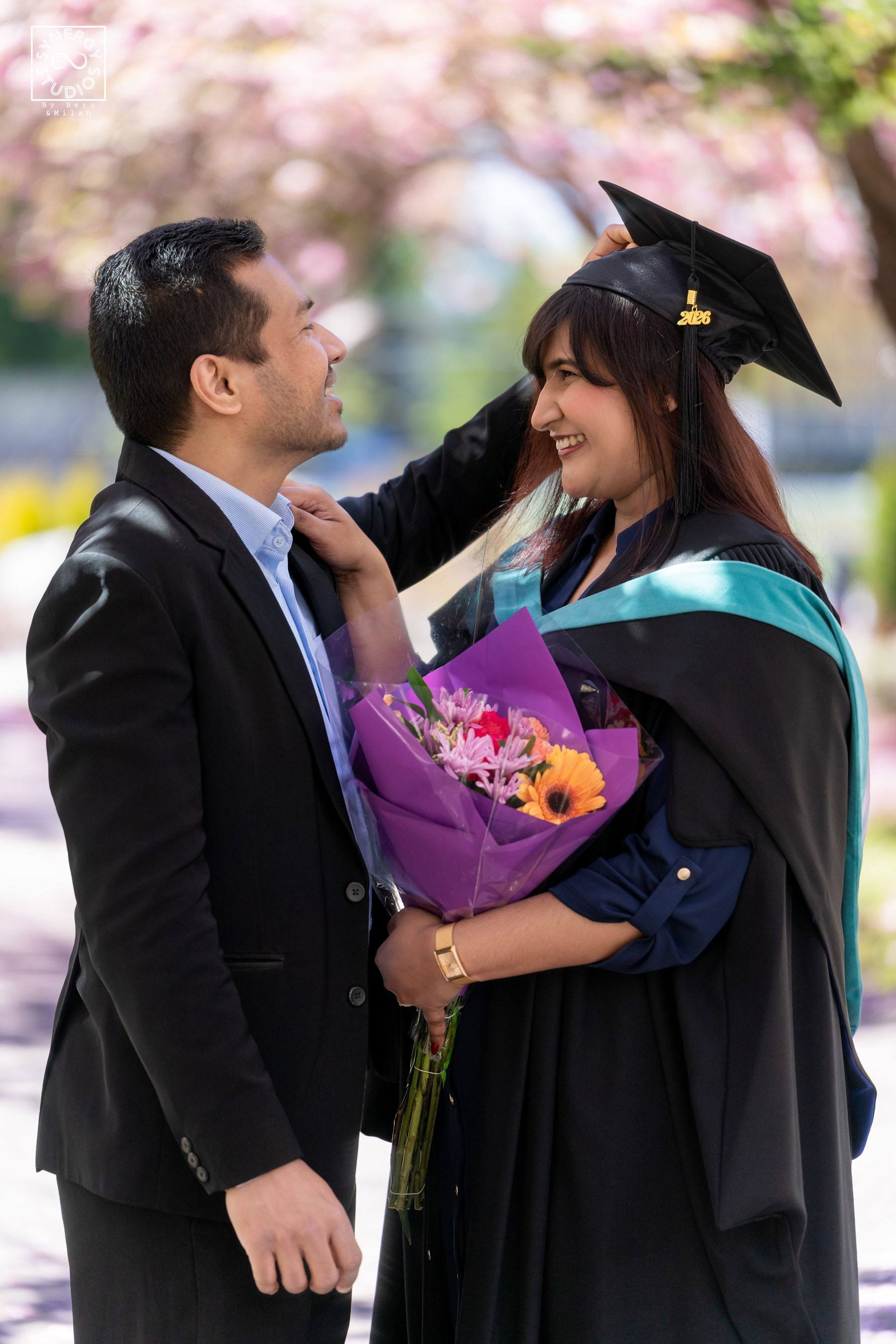 Graduate kissing her husband's cheek while holding a purple bouquet