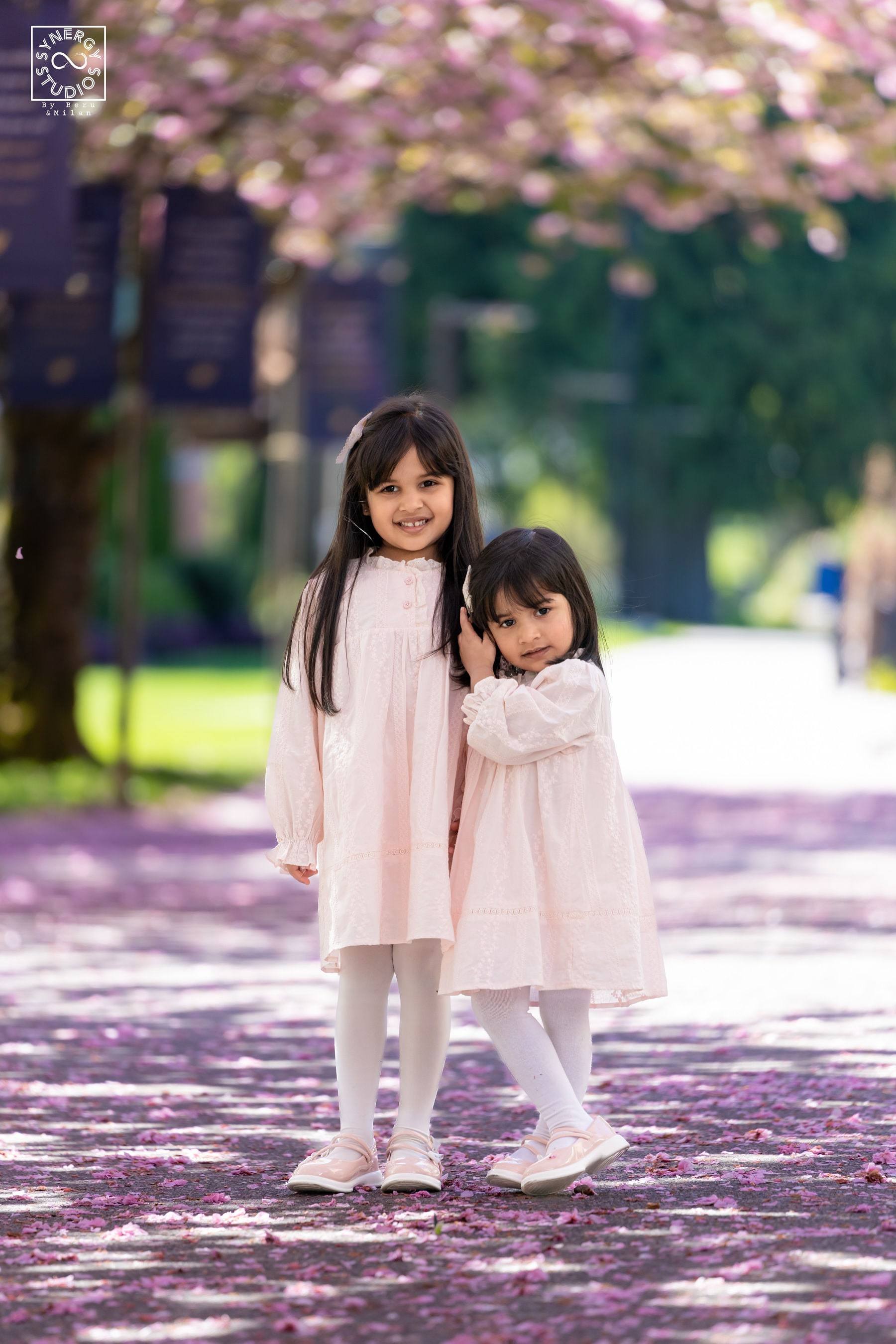 Two young girls holding hands on a blossom-covered walkway