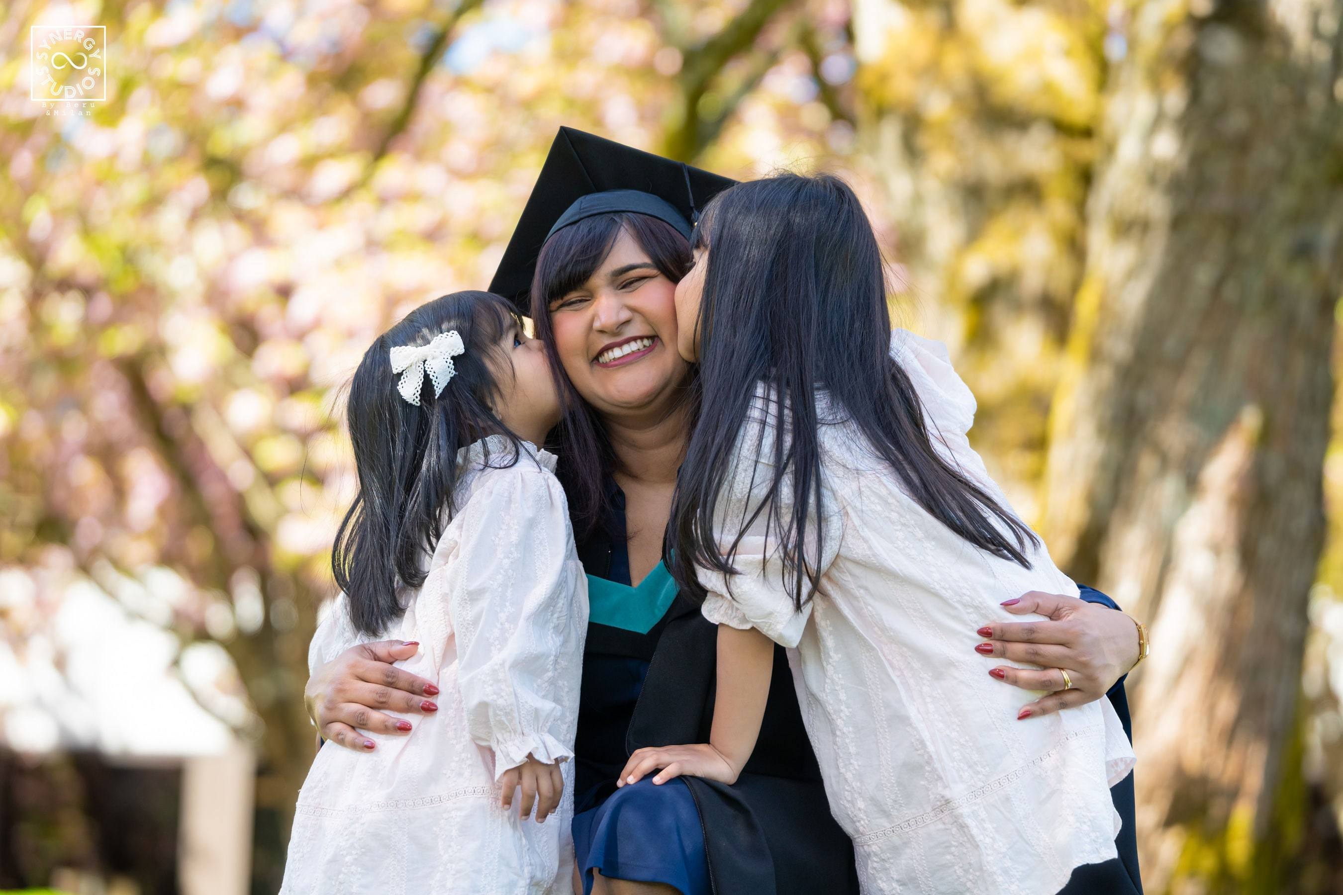 Graduate hugging her two daughters among cherry blossoms