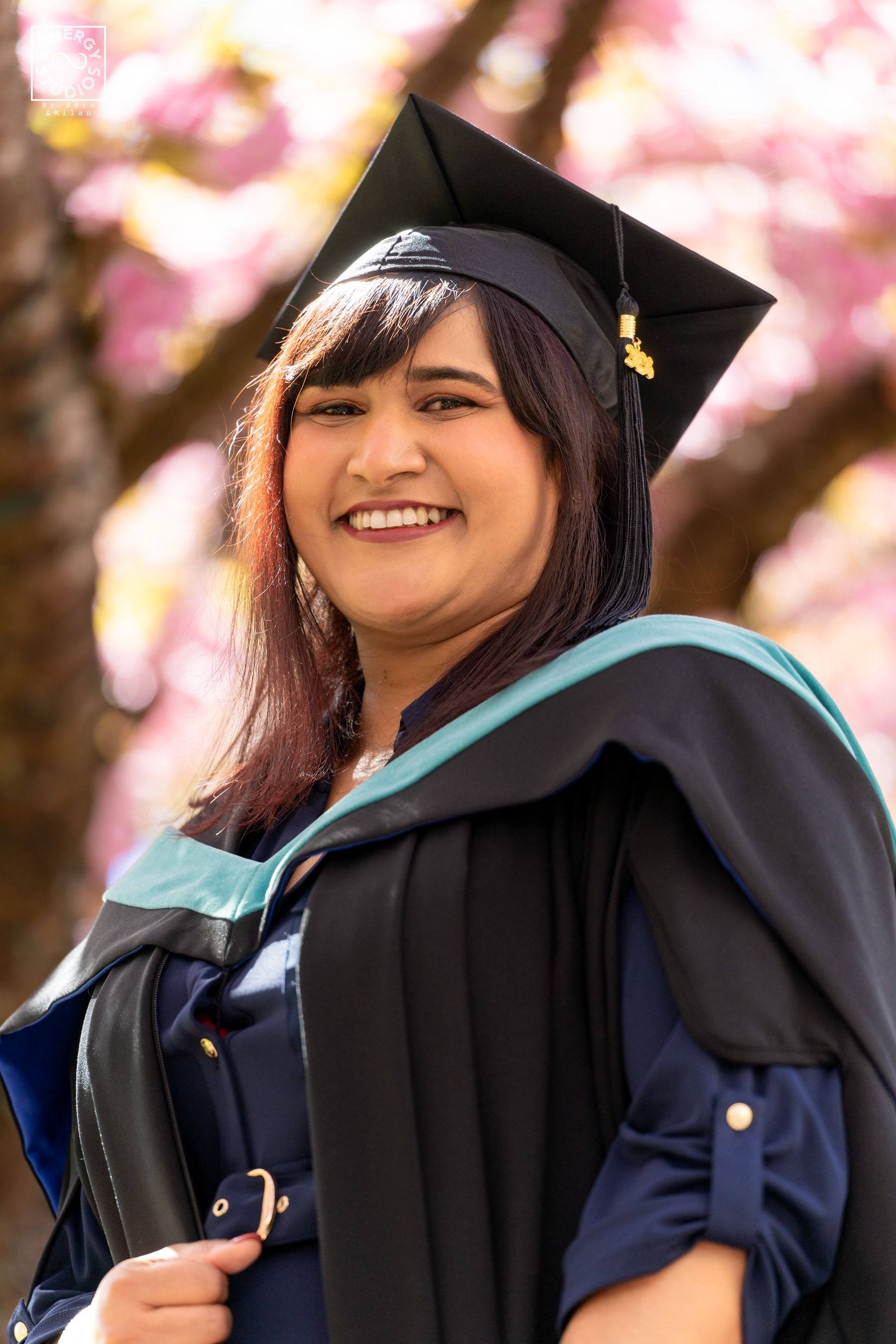 Close portrait of a smiling graduate in cap and hood framed by pink blossoms
