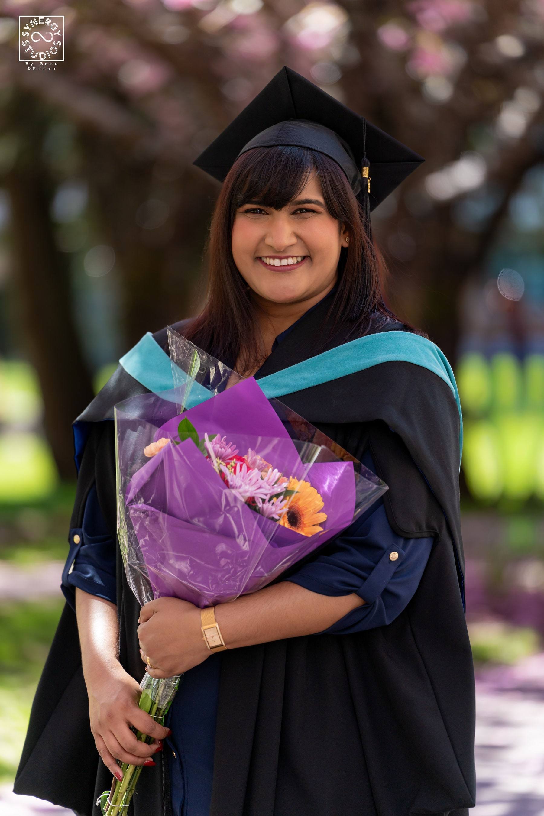 Graduate holding a purple bouquet beneath a cherry blossom canopy