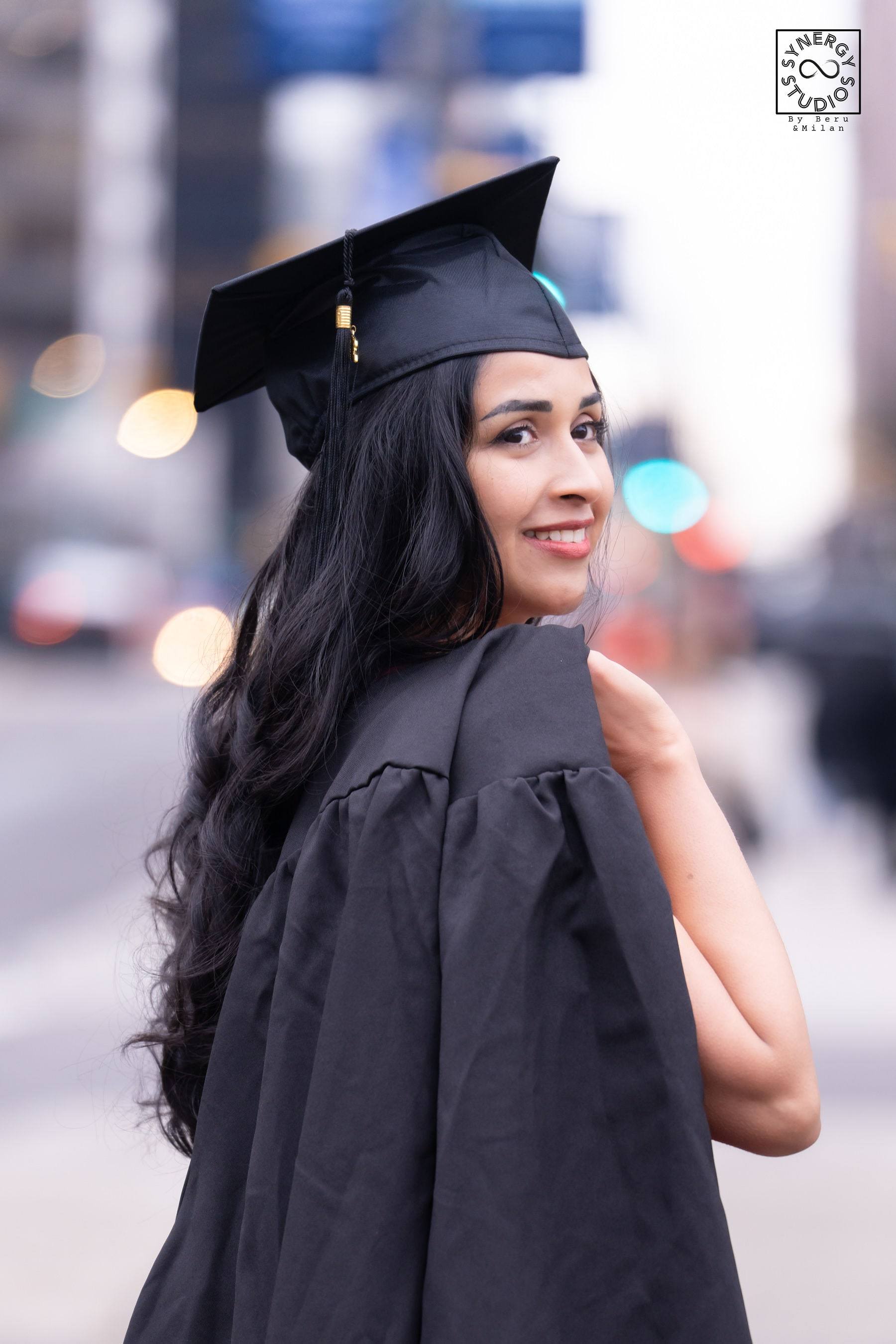 Graduate in a black gown looking back over her shoulder downtown