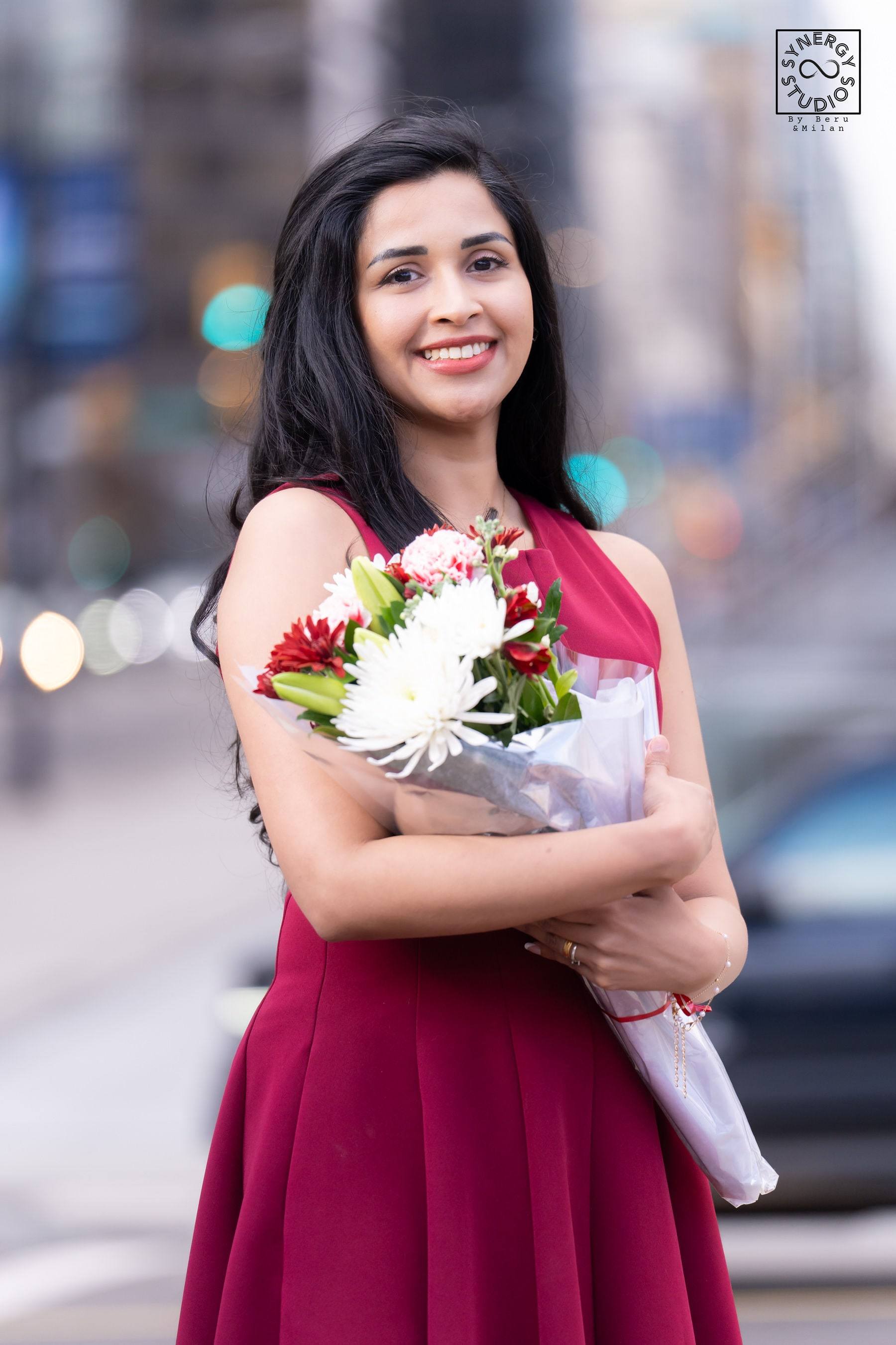 Graduate in a red dress holding a bouquet of roses on a city street
