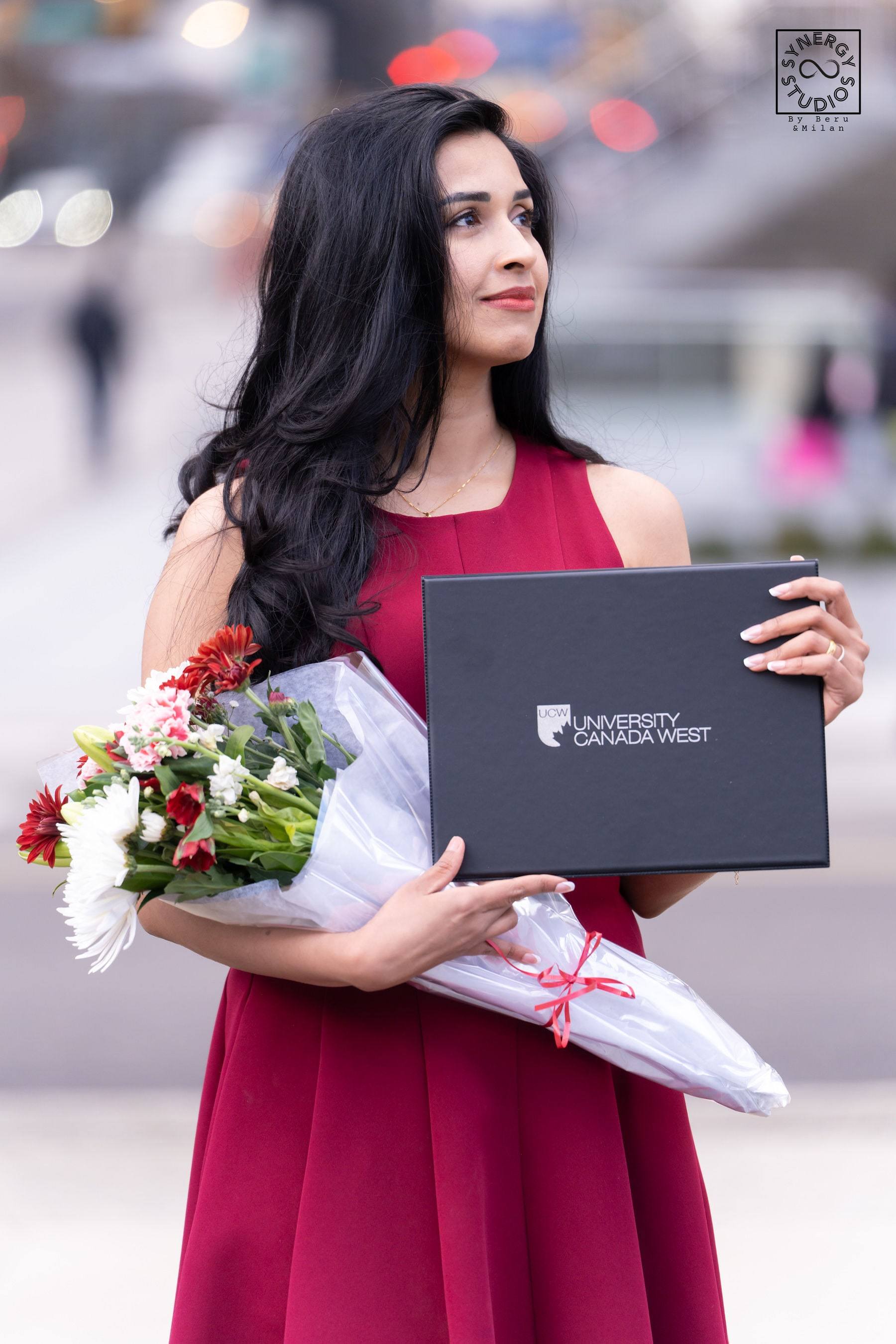 Graduate smiling with her diploma and a bouquet of red and white flowers