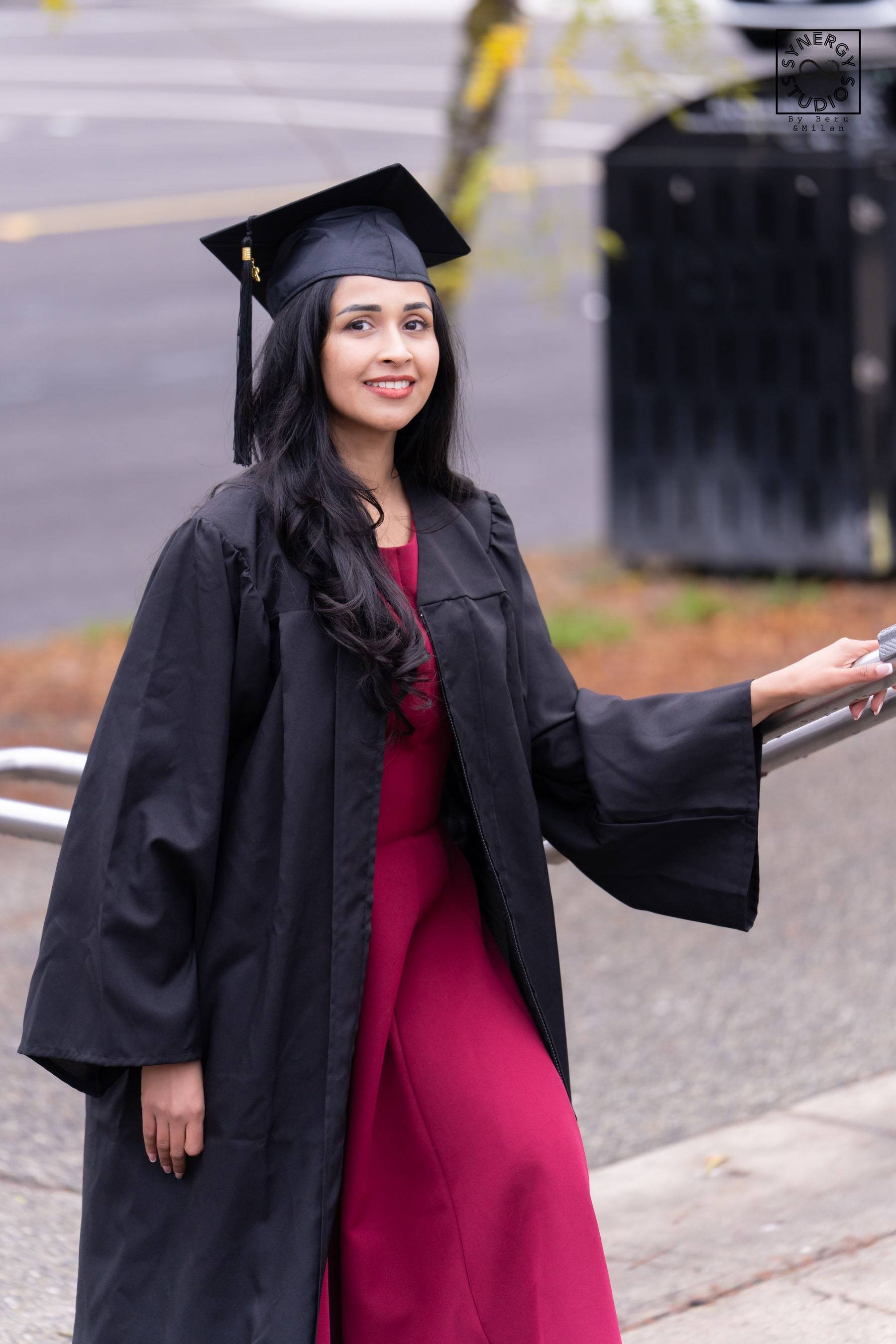 Graduate in a red dress and gown laughing on a downtown sidewalk