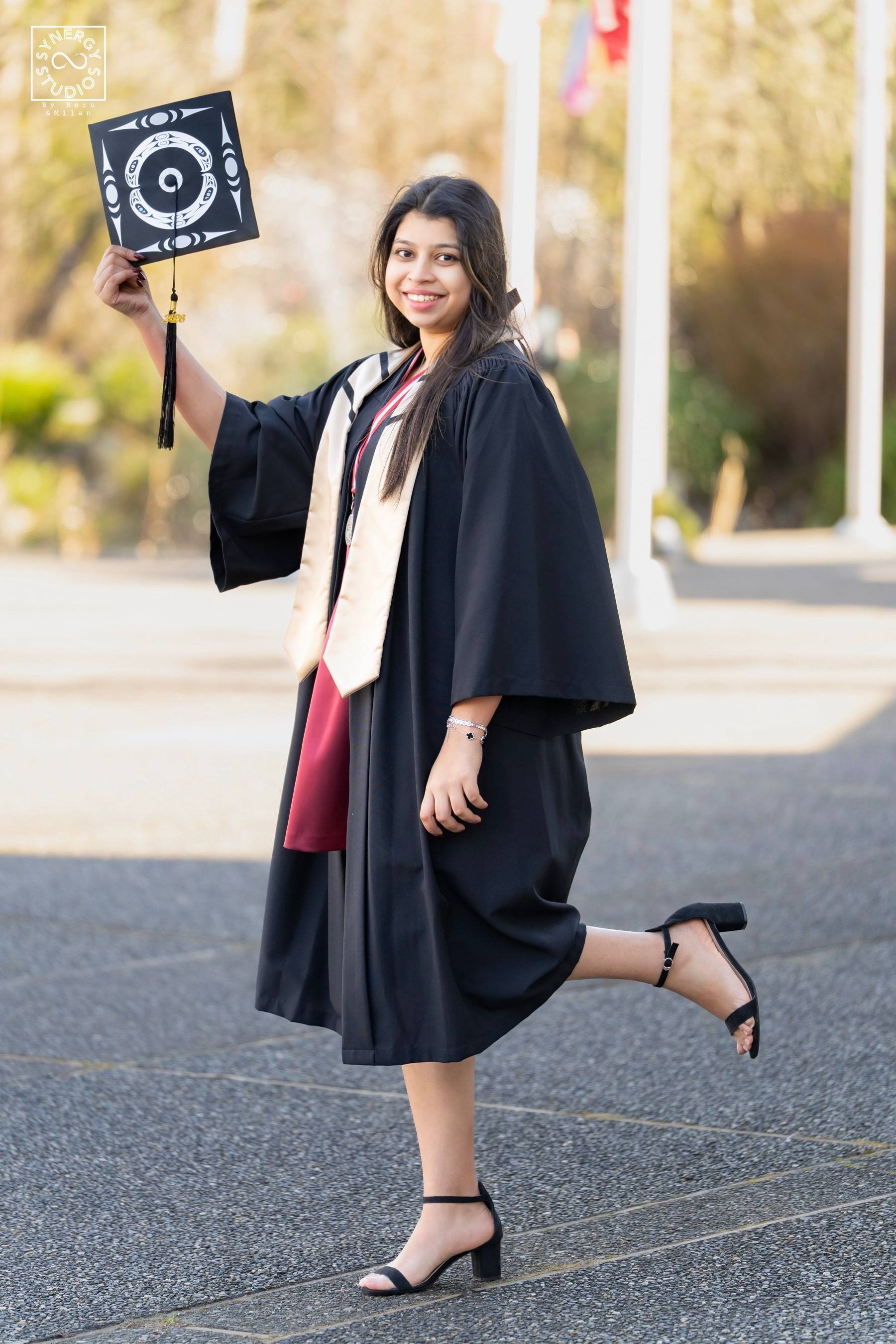 Graduate raising her decorated cap in the air on a campus walkway